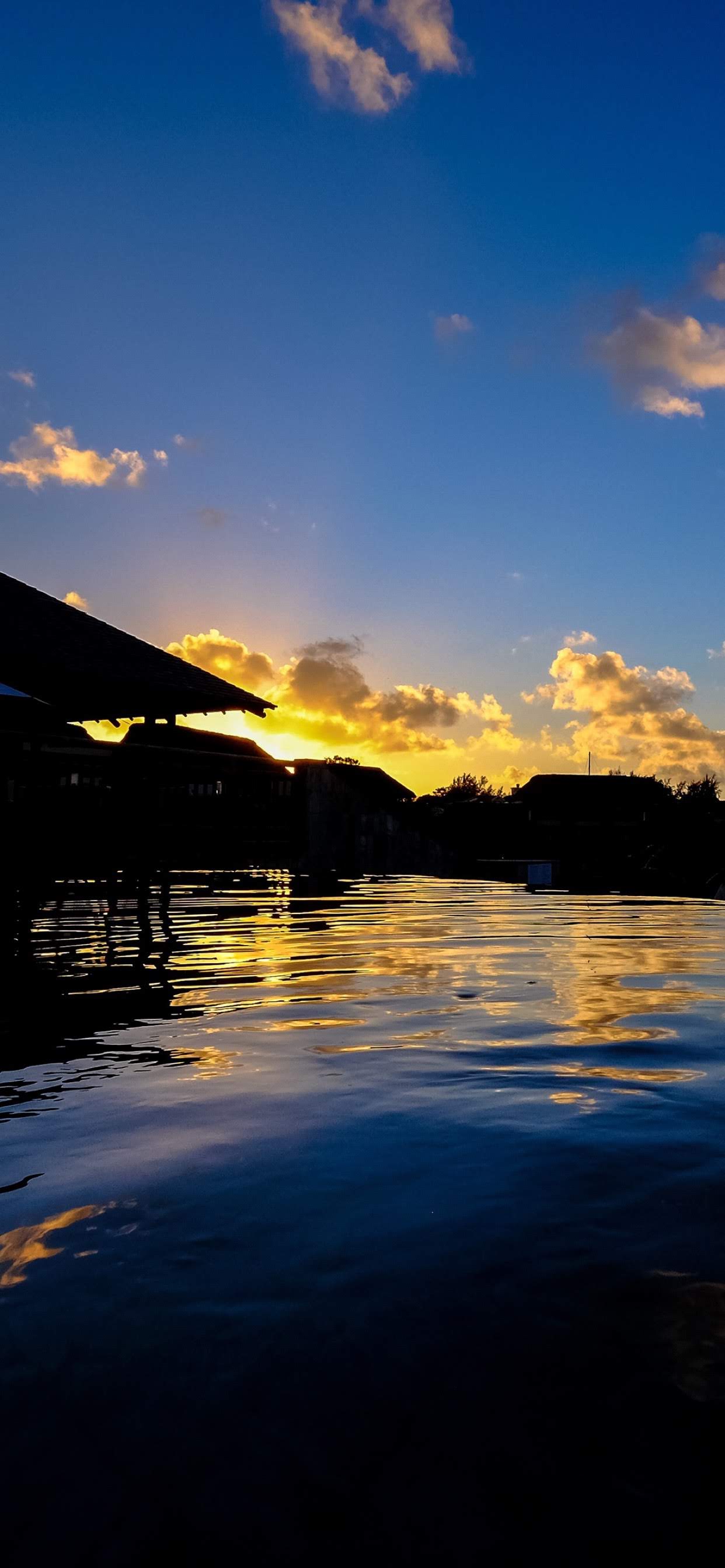 Golden clouds and silhouetted buildings reflected in blue pool water