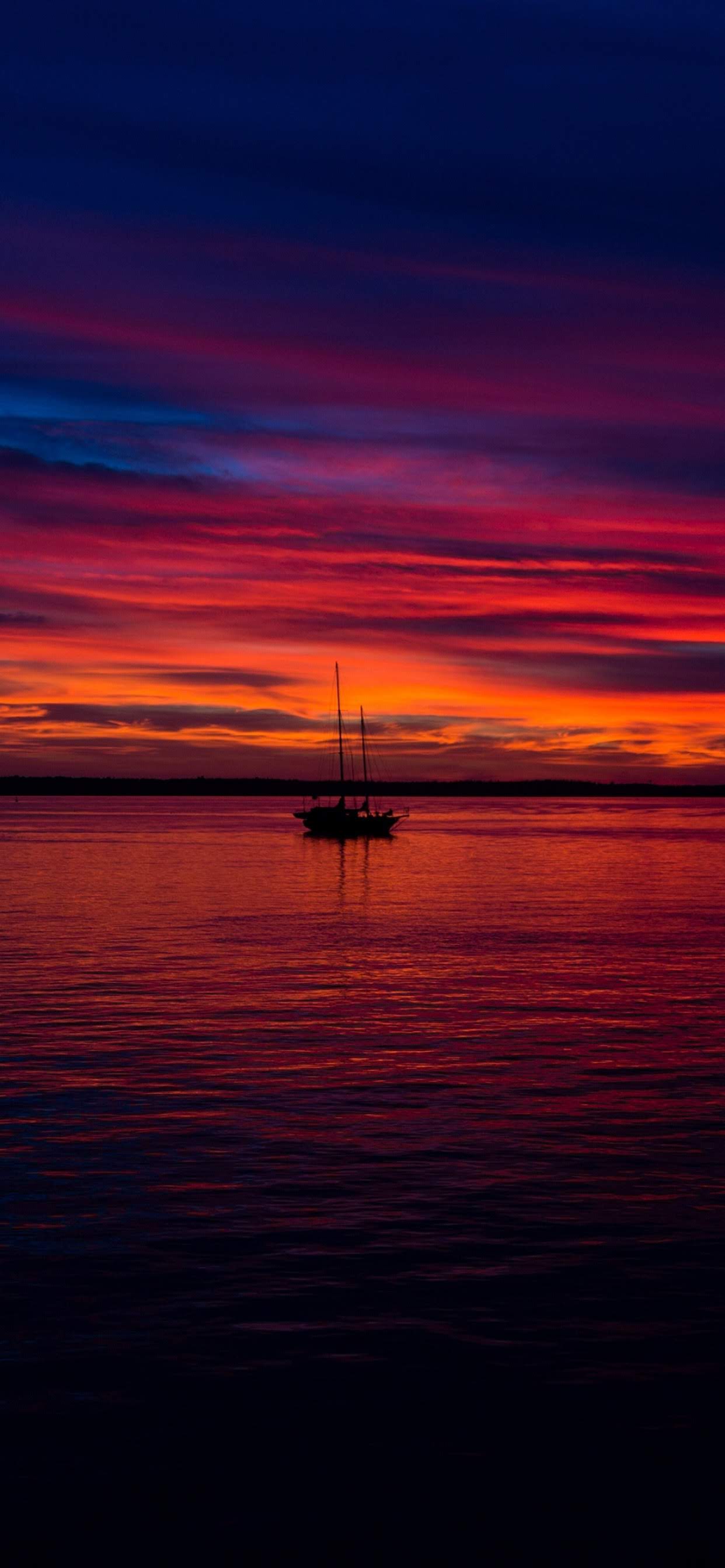 A sailboat silhouetted on calm water beneath a crimson and blue sky
