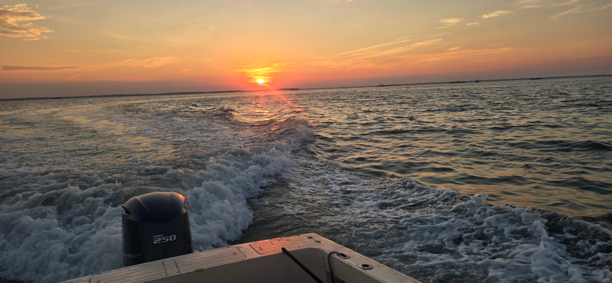 A boat leaving a foamy wake across the water beneath an orange sunset