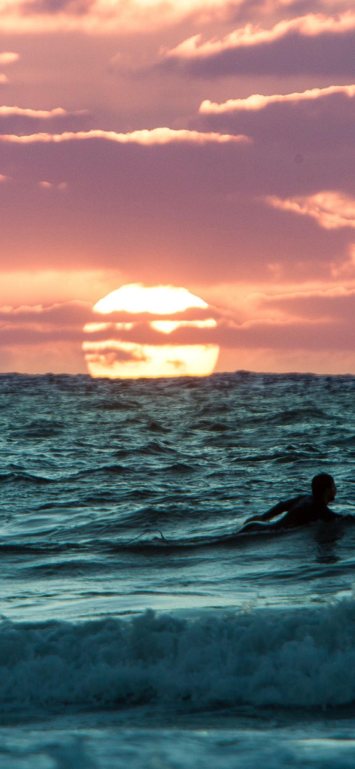 A surfer silhouetted against ocean waves and a large setting sun
